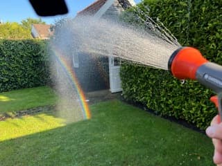 Tuin besproeien na warme dag met prachtige regenboog in de waterstraal