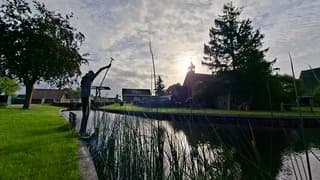 Zon achter kerktorentje, met kunstwerk de melkvaarder op voorgrond