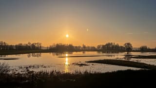 Ondergaande zon boven ondergelopen weiland