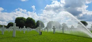 Blauw bewolkte lucht zon en het besproeien van het gras