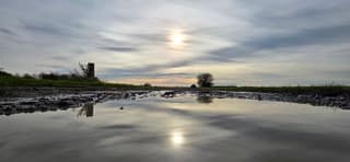Zon sluierbewolking en weerspiegeling in een regenplas 