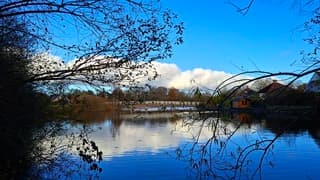 Doorkijk naar wandelbruggetje en wolken weerspiegeld