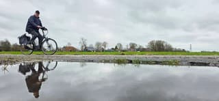 Bewolking en een fietser die weerspiegelt in een regenplas 