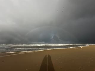 Regenboog voor donkere wolken boven zee