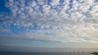Blauwe dag met veel altocumuluswolken en boven zee een beetje mistig
