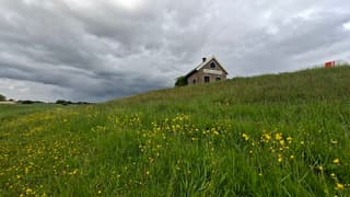 Donkere wolken/bui hangt achter de heuvel met dijkhuisje in dit veld tussen de gele boterbloemen