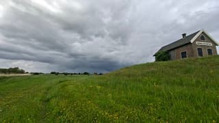 Donkere wolken/bui hangt achter de heuvel met dijkhuisje in dit veld tussen de gele boterbloemen