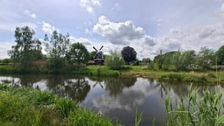 Molen langs riviertje met stapelwolken en zon