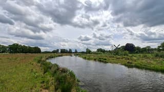 Zon, stapelwolken, bootje, molen en riviertje